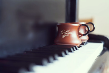Cup of coffee on an old piano keyboard while composing. Evening time and some sun rays. Coffee mug on the piano keyboard