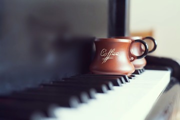 Cup of coffee on an old piano keyboard while composing. Evening time and some sun rays. Coffee mug...