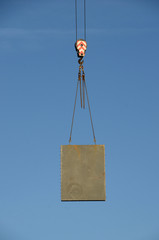 Concrete element hangs in chains from a crane.