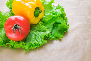 Fresh yellow paprika, tomatoes and green salad leaves on a grey background. Space for text. Healthy eating concept.