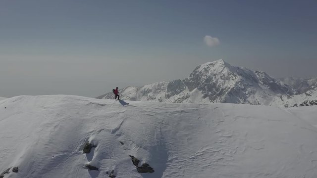 Mountaineer stands on a snowy mountain ridge. European Alps, Italy. 4K UHD Log native file, aerial shot.