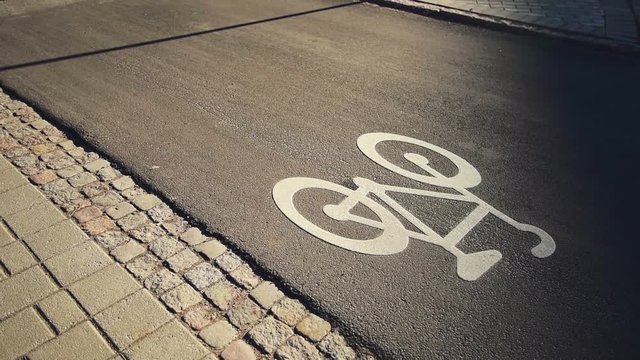 Bicycle ride on urban lane in sunset, shadow of unrecognizable cyclist riding a bike through city street next to the road marking