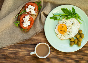 Fried eggs, a sandwich with vegetables and feta cheese and cappuccino coffee for breakfast. Tomatoes and bread on a wooden table