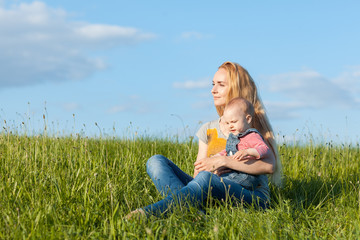 Fototapeta premium Young mother sitting in the grass and holding a child