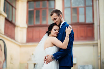 Happy groom kisses his beloved forehead against the background of the wall