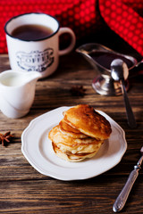 Hearty and tasty breakfast or lunch, fried pancakes with strawberry jam, milk and black tea on a dark wooden background 