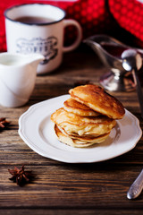 Hearty and tasty breakfast or lunch, fried pancakes with strawberry jam, milk and black tea on a dark wooden background 