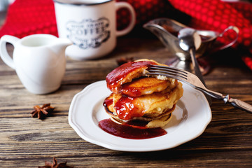 Hearty and tasty breakfast or lunch, fried pancakes with strawberry jam, milk and black tea on a dark wooden background 