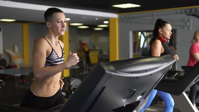 A sportswoman is intensively running on a treadmill in a fitness club, in order to maintain her muscles in tonus. The correct position of the hands helps to increase the speed during training.