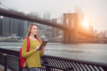 Beautiful young student girl walking in the city with backpack using tablet pc outdoors in New York City