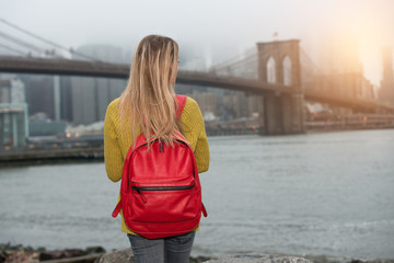 Young tourist woman traveling in New New York city with red backpack and looking to Brooklyn Bridge.