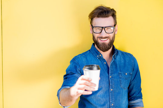 Portrait of a handsome man in blue t-shirt standing with coffee to go on the yellow background