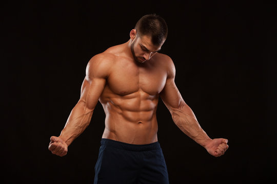 Strong Athletic Man Fitness Model Torso showing six pack abs. isolated on black background with copyspace is looking at himself