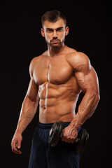 Fototapeta na wymiar Handsome power athletic man with dumbbell is confidently looking forward. Strong bodybuilder with six pack, perfect abs, shoulders, biceps, triceps and chest Isolated on black background with