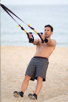 Athletischer Mann macht TRX Training am Strand