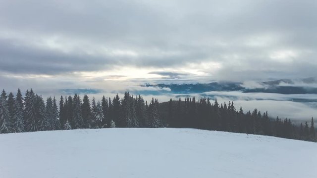 4k winter mountains with clouds and fog in sunset time. Ski slope, pine tree forest, mount range in the background. Majestic nature landscape. Holidays in Ski Resort Bukovel, Ukraine. Time lapse