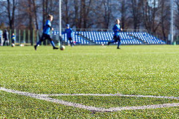 Obraz na płótnie Canvas Football field corner green turf, blurred young soccer players on background