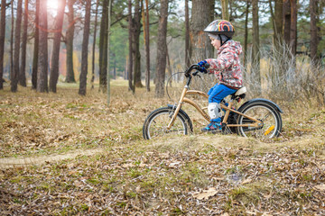 Naklejka premium child on a bicycle in the forest in early morning. Boy cycling outdoors in helmet