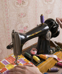 Old vintage hand sewing machine with color thread spools, fabric and scissors on the pink background.
