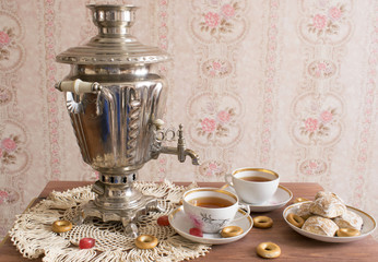Russian traditional samovar and cups of tea with cookies on the table next to the pink wall.