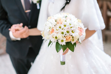 Wedding bouquet from fresh spring flowers. Bride holding white wedding bouquet close up. The groom holding by a hand the bride in a white wedding dress. marriage concept.