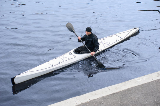 A man in a white kayak near the city riverbank