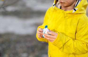 Little boy in a yellow raincoat playing with Easter eggs