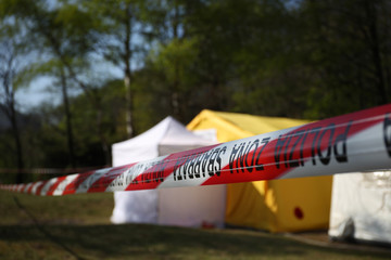 Red and white police line around a crime scene tent in a forest