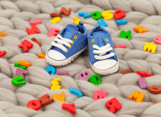 photo of little child shoes near colorful letters on the wonderful grey blanket background
