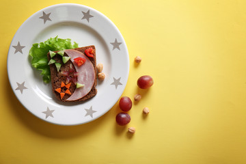 Plate with creative sandwich and grape on yellow background