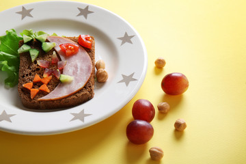Plate with creative sandwich and grape on yellow background