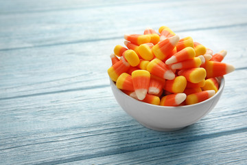Colorful Halloween candy corns in bowl on wooden background