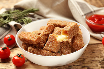 Bowl of tasty cheese sticks and tomatoes on wooden background