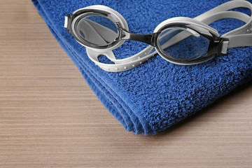 Swimming goggles with towel on wooden background