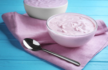 Tasty yogurt in bowl with spoon on wooden table
