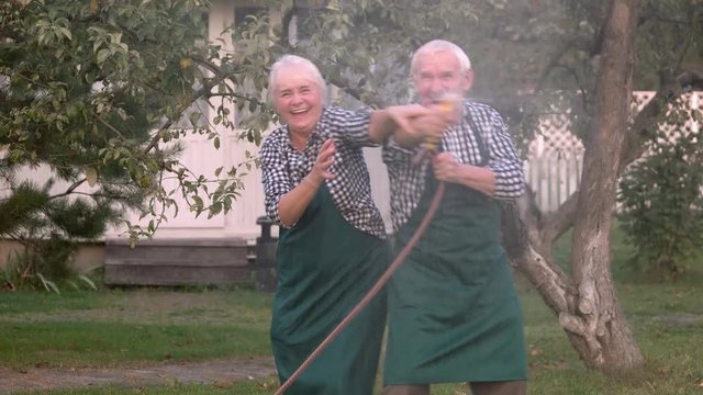 Elderly couple with garden hose. Old people having fun.