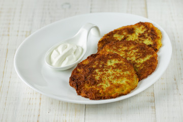 Potato pancakes on a white plate with sour cream