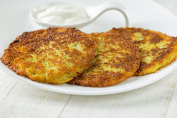 Potato pancakes on a white plate with sour cream