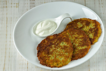 Potato pancakes on a white plate with sour cream
