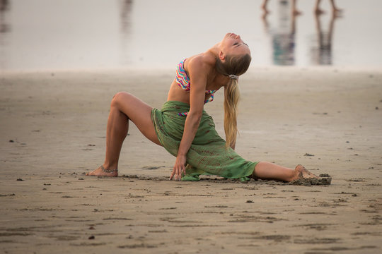 Pose Ashva sanchalanasana. A young woman in a bikini is engaged in yoga on the beach.