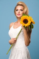 Portrait of attractive summer woman with sunflower in hand on blue background