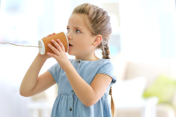 Cute little girl using plastic cup as telephone while playing at home