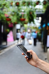 Closeup of male hand using smartphone in city street. Business man typing text message or playing video games on mobile phone screen in urban background.