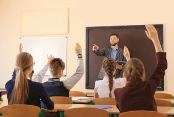 Pupils listening teacher and raising hands to answer in classroom