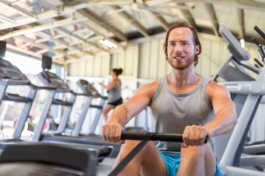 Man Athlete Training Cardio On Rowing Machine In Fitness Gym.