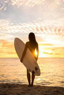 Beach sunset sexy surfer woman surfing lifestyle relaxing holding surfboard looking at ocean for surf. Active healthy living silhouette of sports athlete standing waiting for waves.