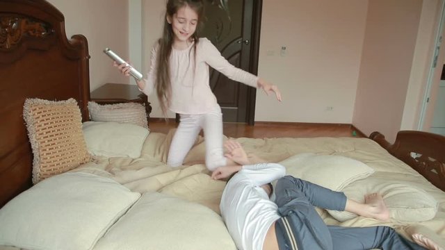 Brother and sister fights and pushes each other at home in the parents' bedroom. fighting for the phone