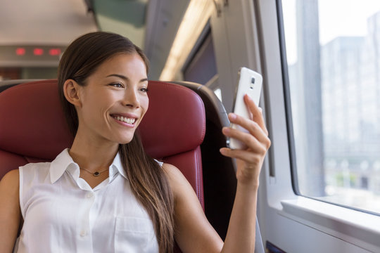 Asian woman using smartphone app taking pictures of the view while traveling in train. Happy young lady watching video holding mobile phone during transport on travel vacation.