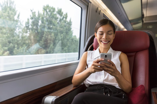 Smiling Asian businesswoman using smartphone social media app while commuting to work in train. Woman sitting in transport enjoying travel.