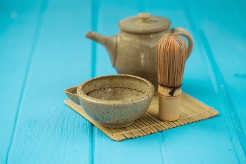 Ceramics bowl and chasen - special bamboo matcha tea whisk, lying on blue wooden background.
